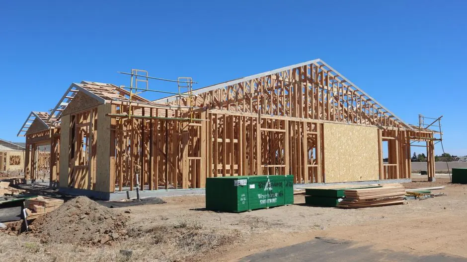 Wooden house frame construction under clear blue sky, sunny day.